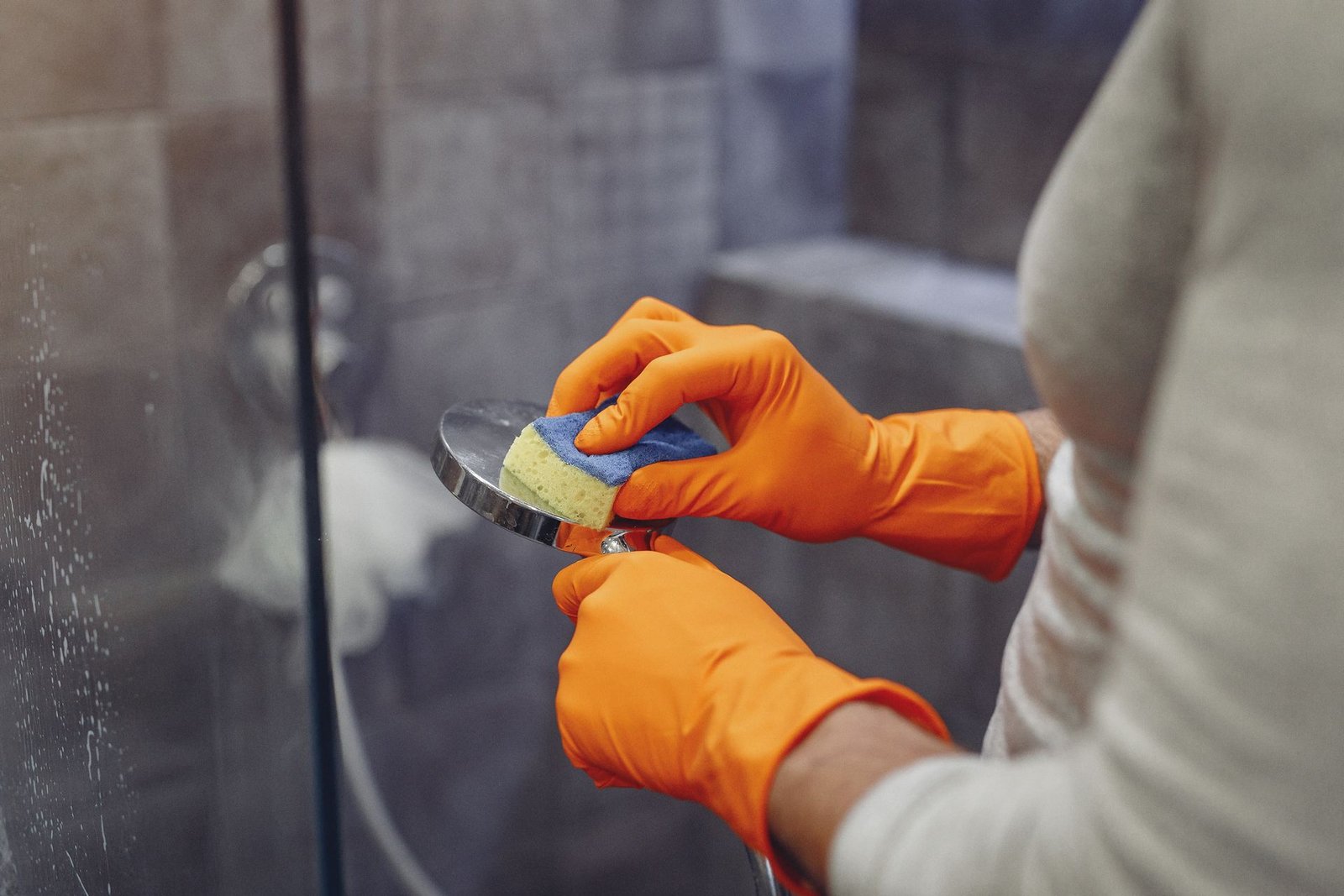 Crop faceless male in orange rubber gloves wiping by sponge showe