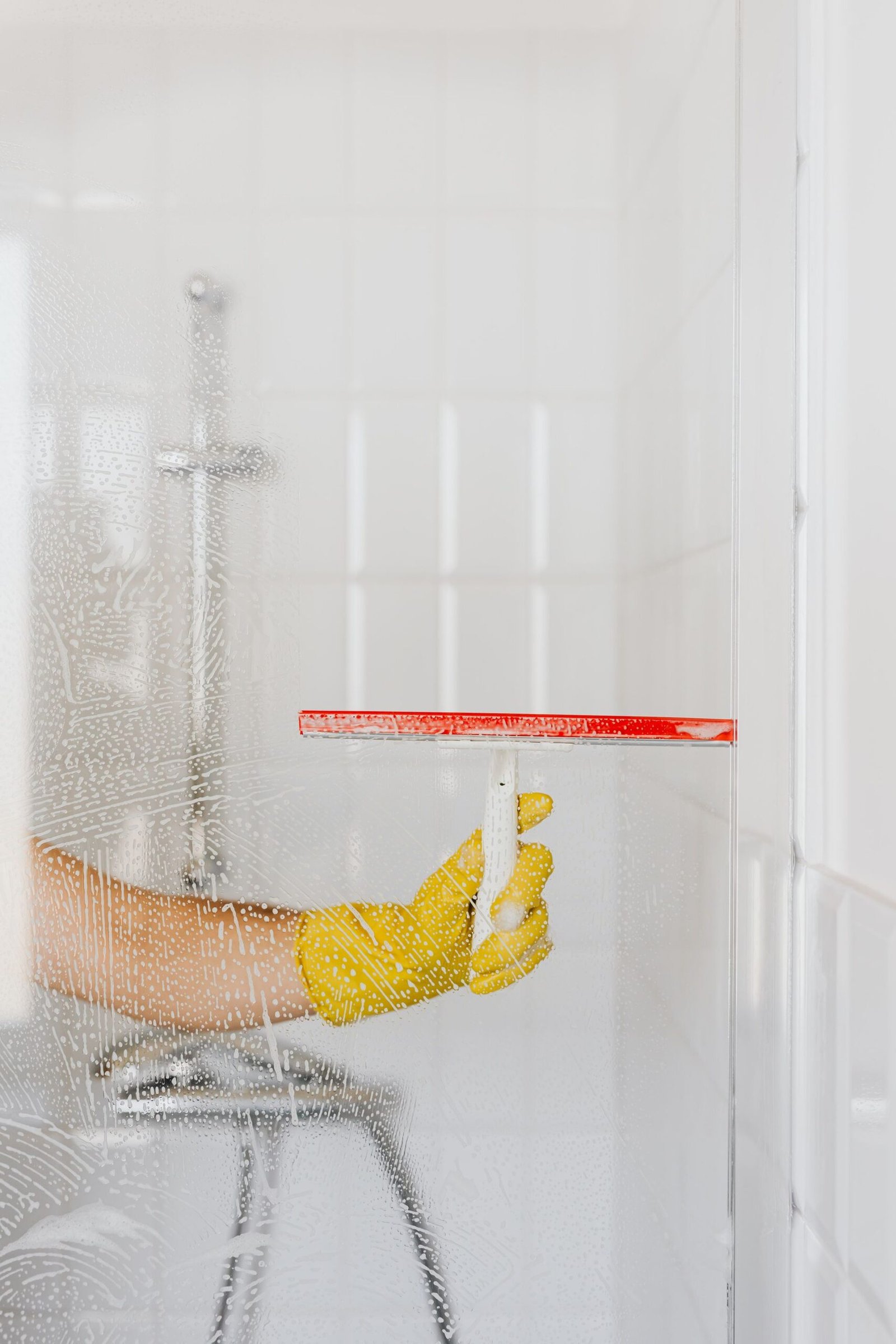 Crop anonymous person in yellow rubber glove cleaning glass showe