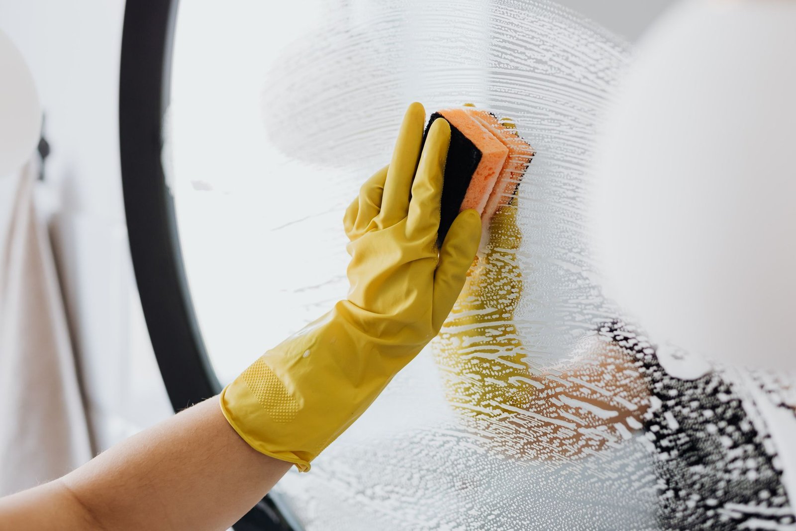 Anonymous person in yellow rubber gloves using simple sponge for