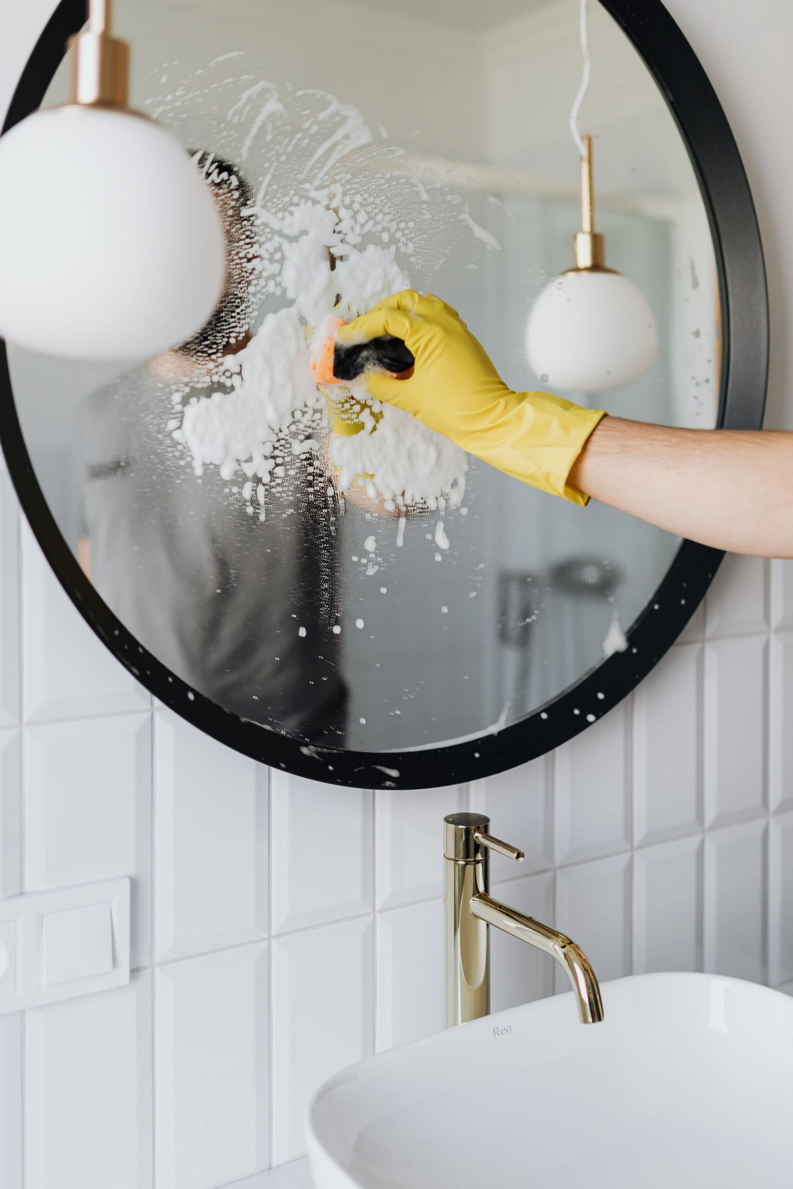 Anonymous housekeeper in yellow rubber gloves wiping round mirror