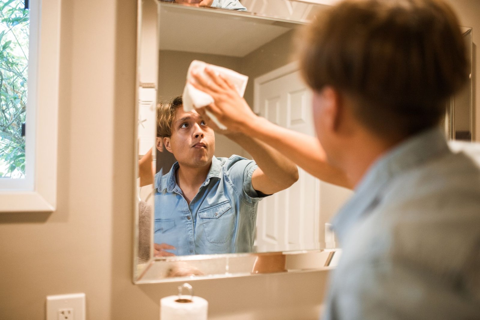 A man wiping a bathroom mirror, focusing on cleanliness and hygie