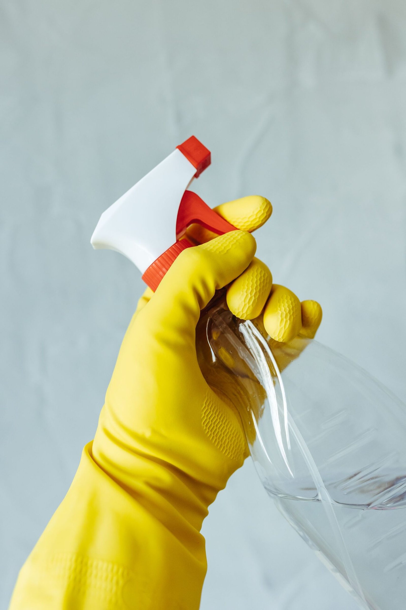 A hand wearing a yellow rubber glove holds a red and white spray
