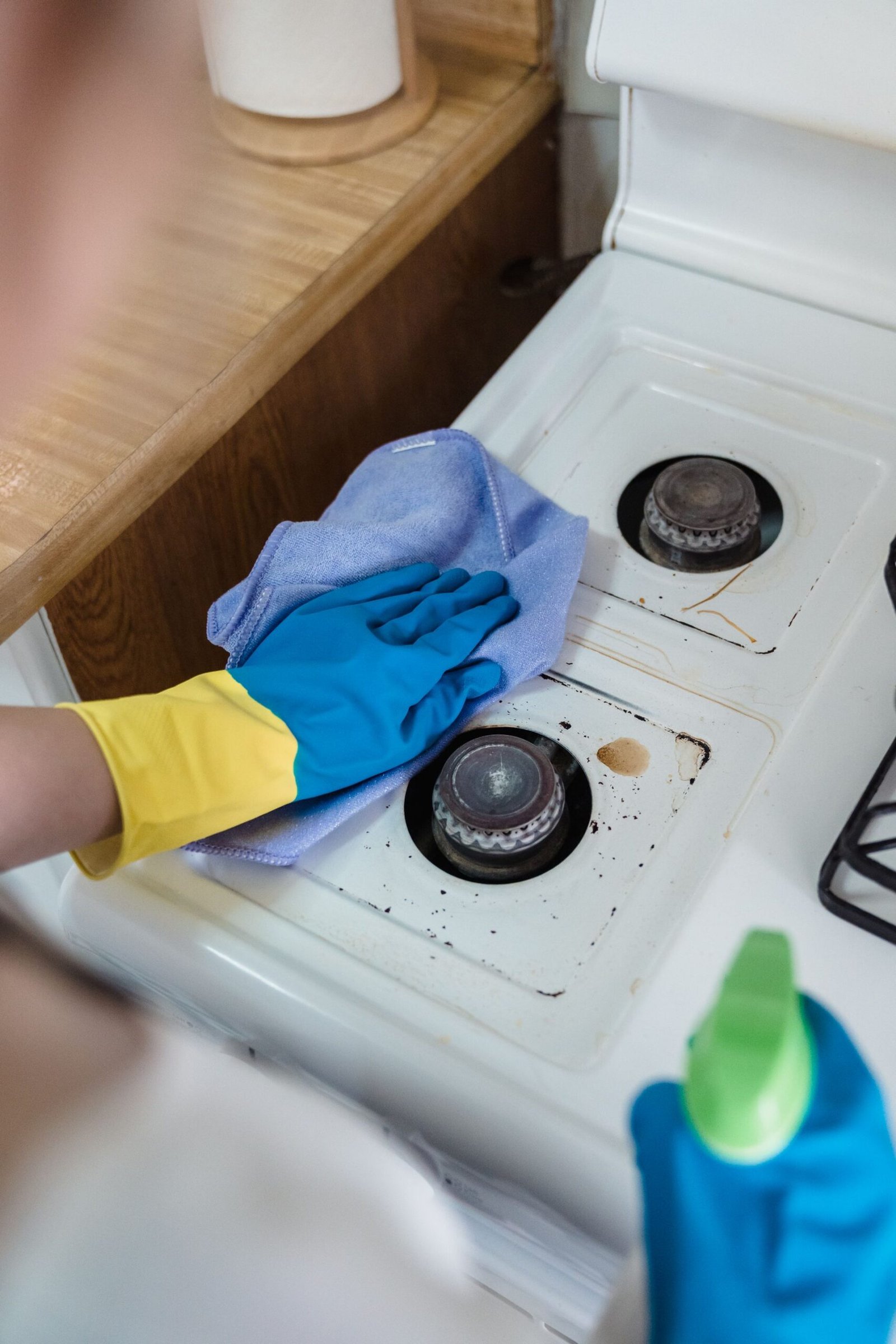 A person wearing rubber gloves cleaning a dirty gas stove with a