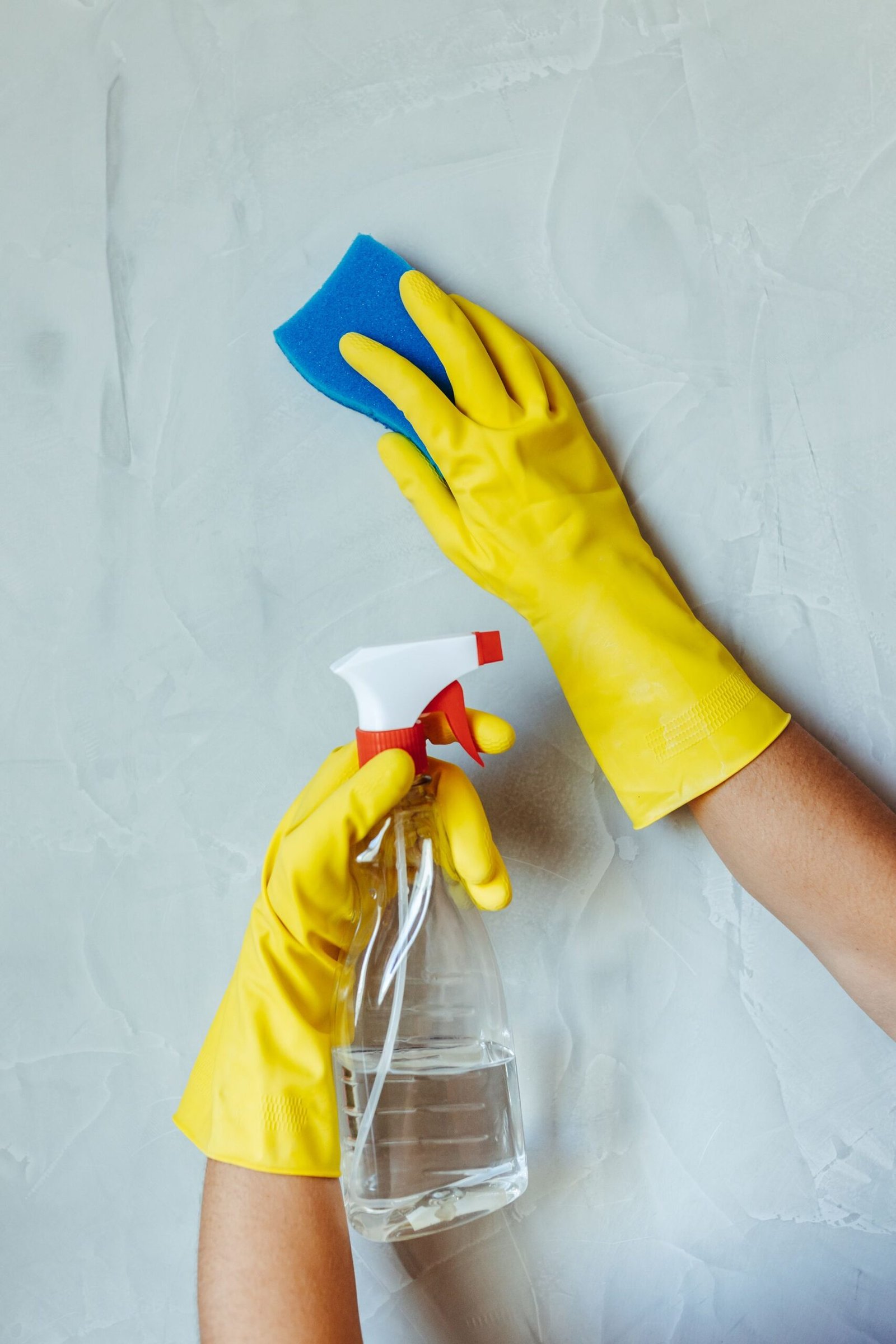 Hands in yellow gloves cleaning wall with sponge and spray bottle