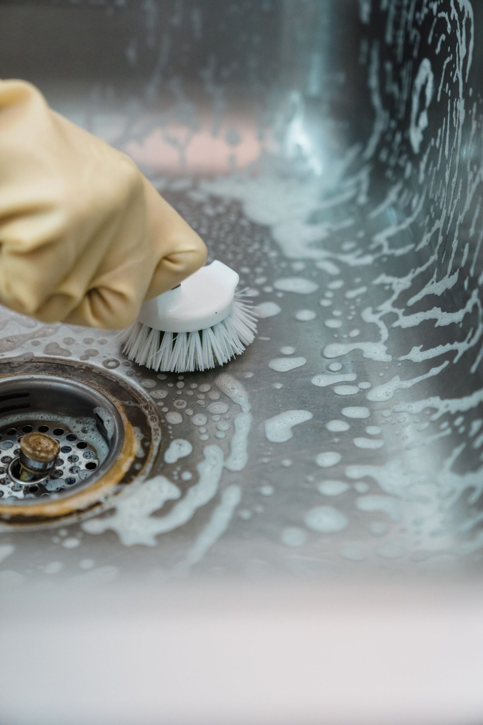 Close-up of a hand in gloves scrubbing a soapy kitchen sink with