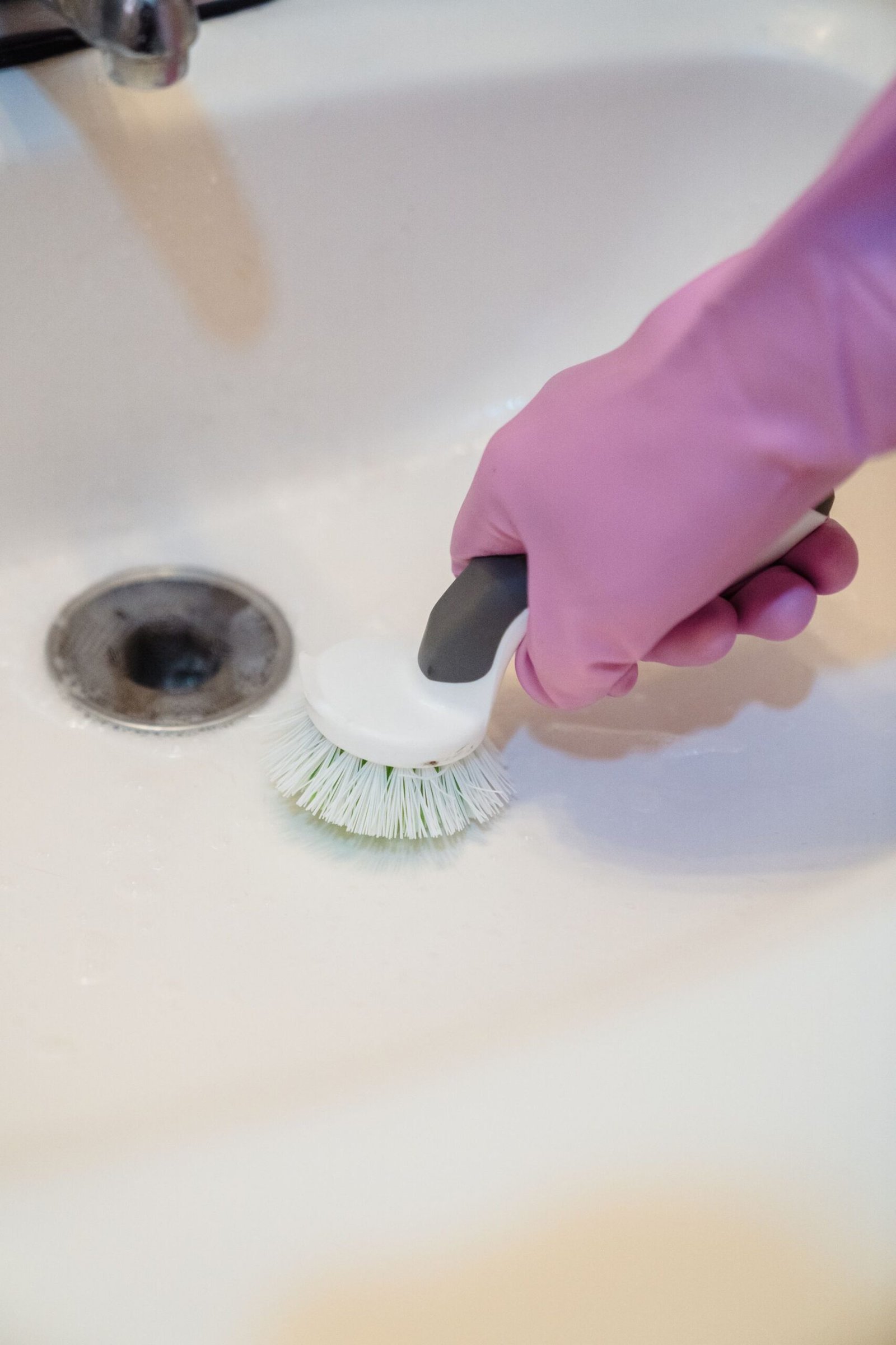A close-up of a hand in a glove cleaning a sink with a scrub brus