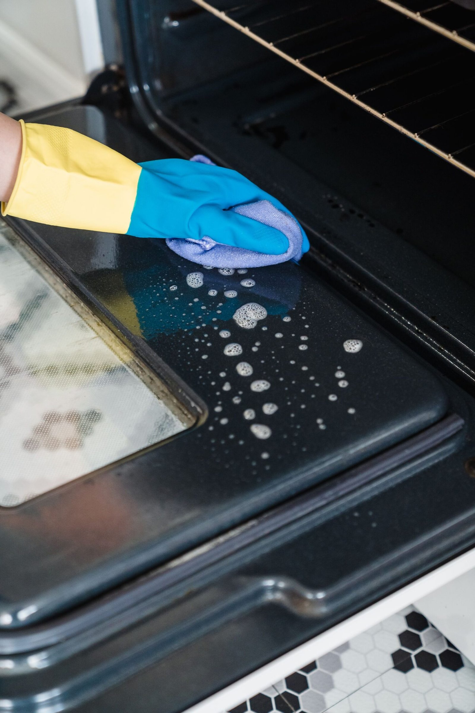 Close-up of cleaning an oven door with gloves and detergent in a