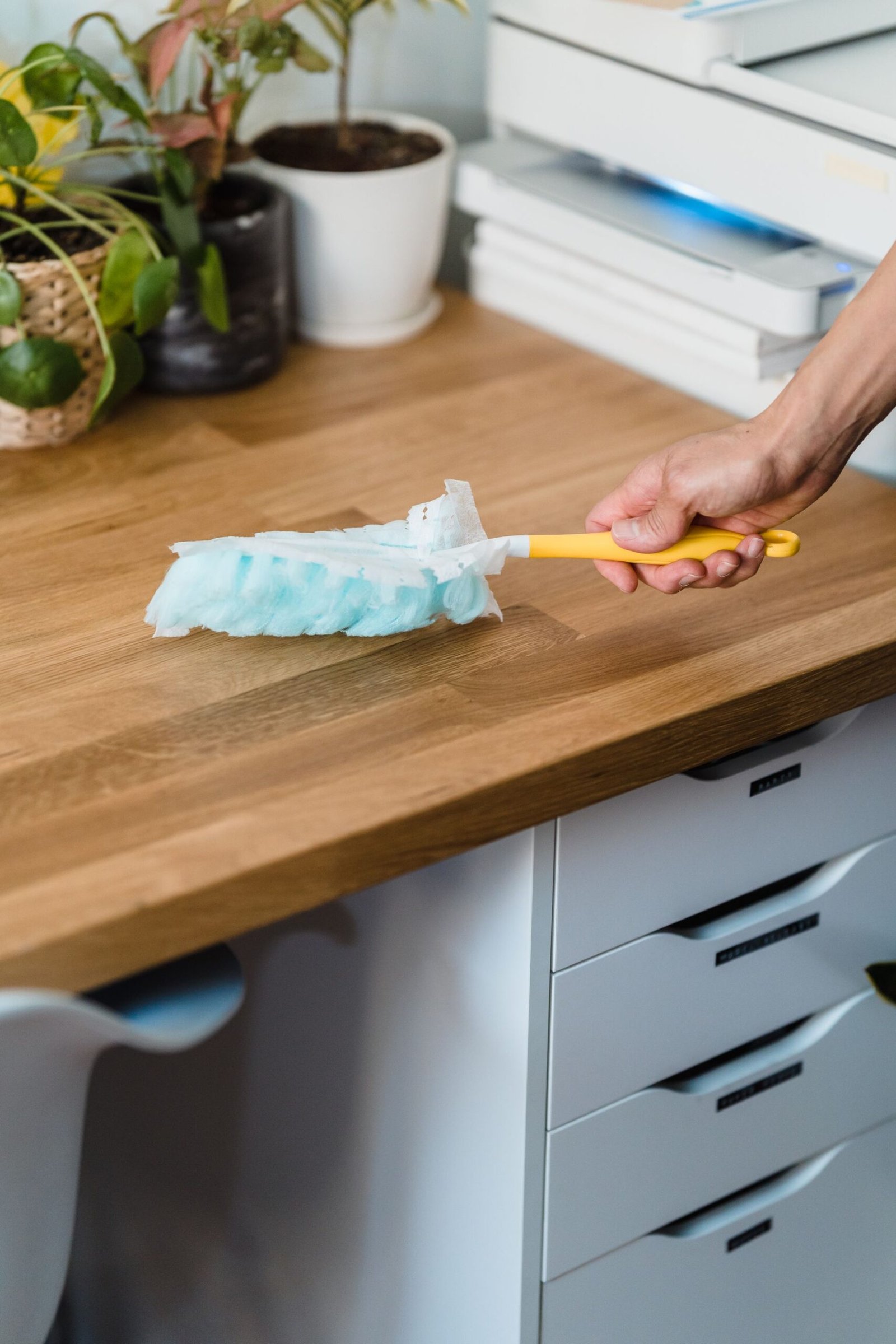 A hand using a feather duster to clean a wooden desk, surrounded