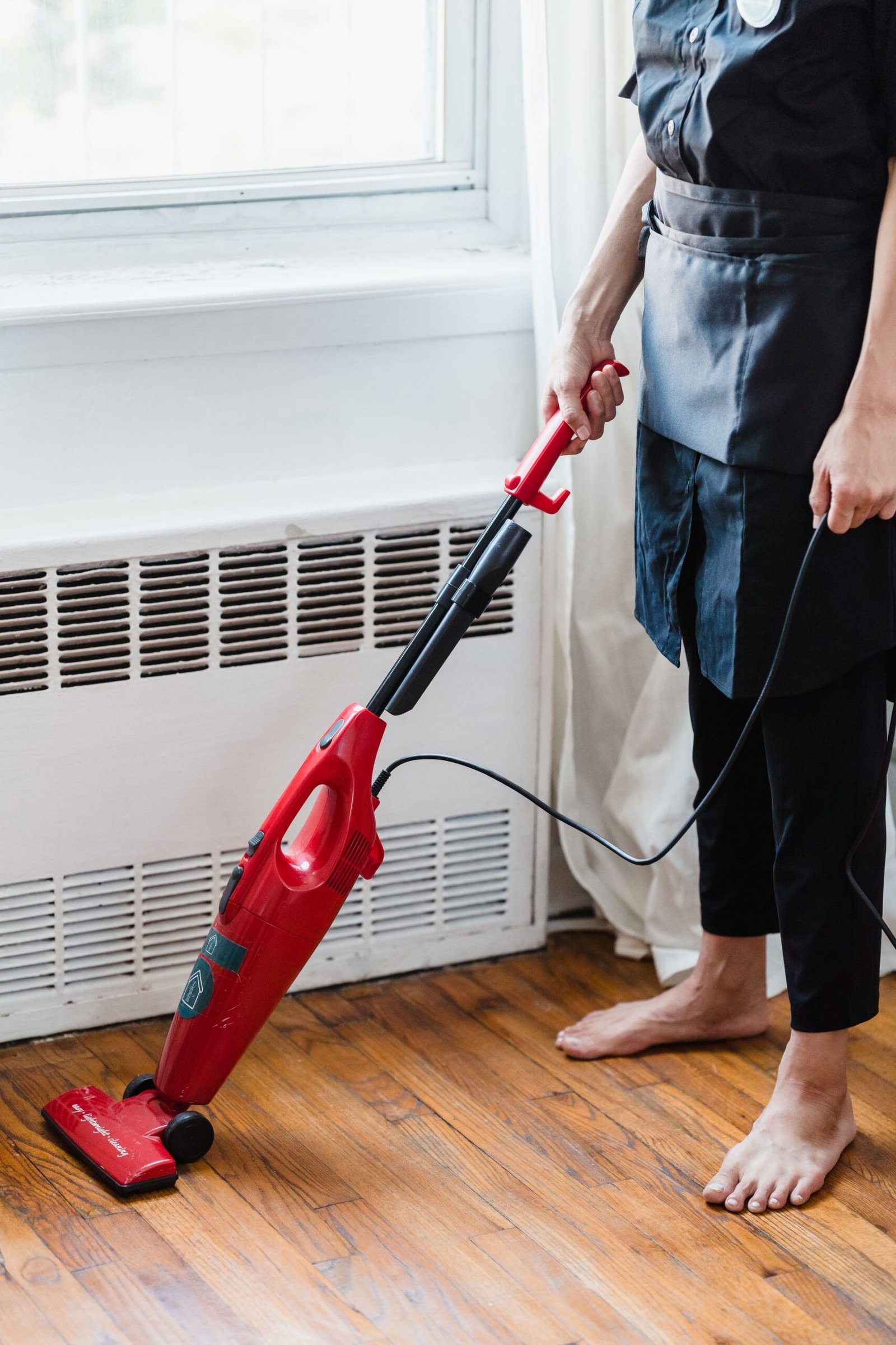 Person cleaning wooden floor with red vacuum cleaner in a well-li