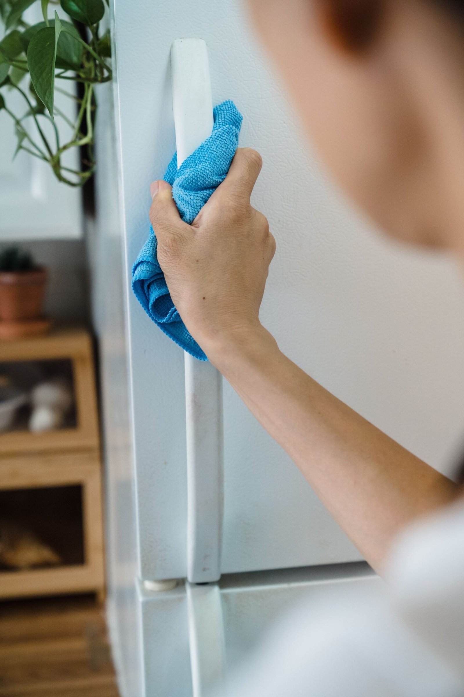 Close-up of a person cleaning a fridge handle with a blue cloth i