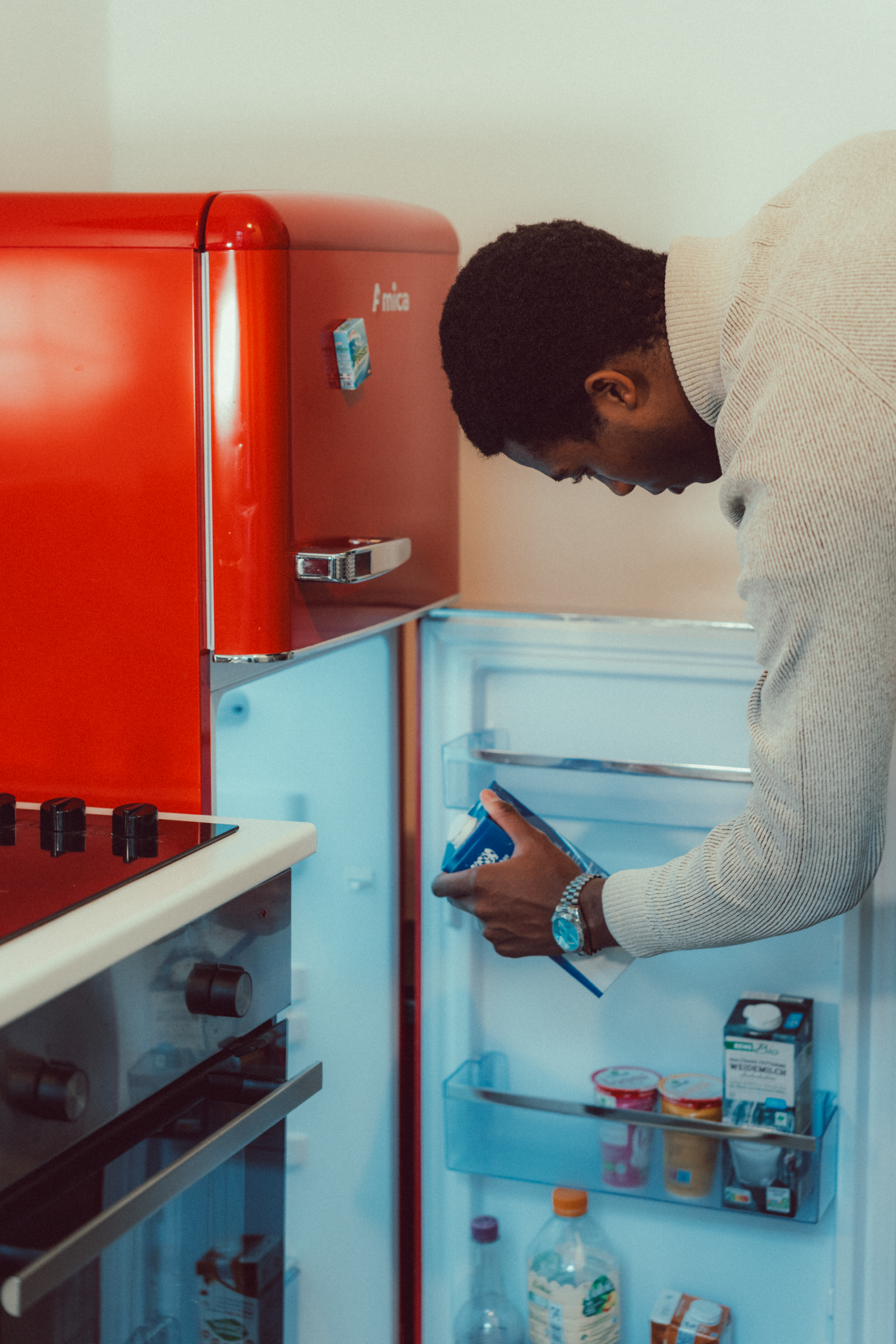 A man looks inside a red fridge, checking food items in a contemp