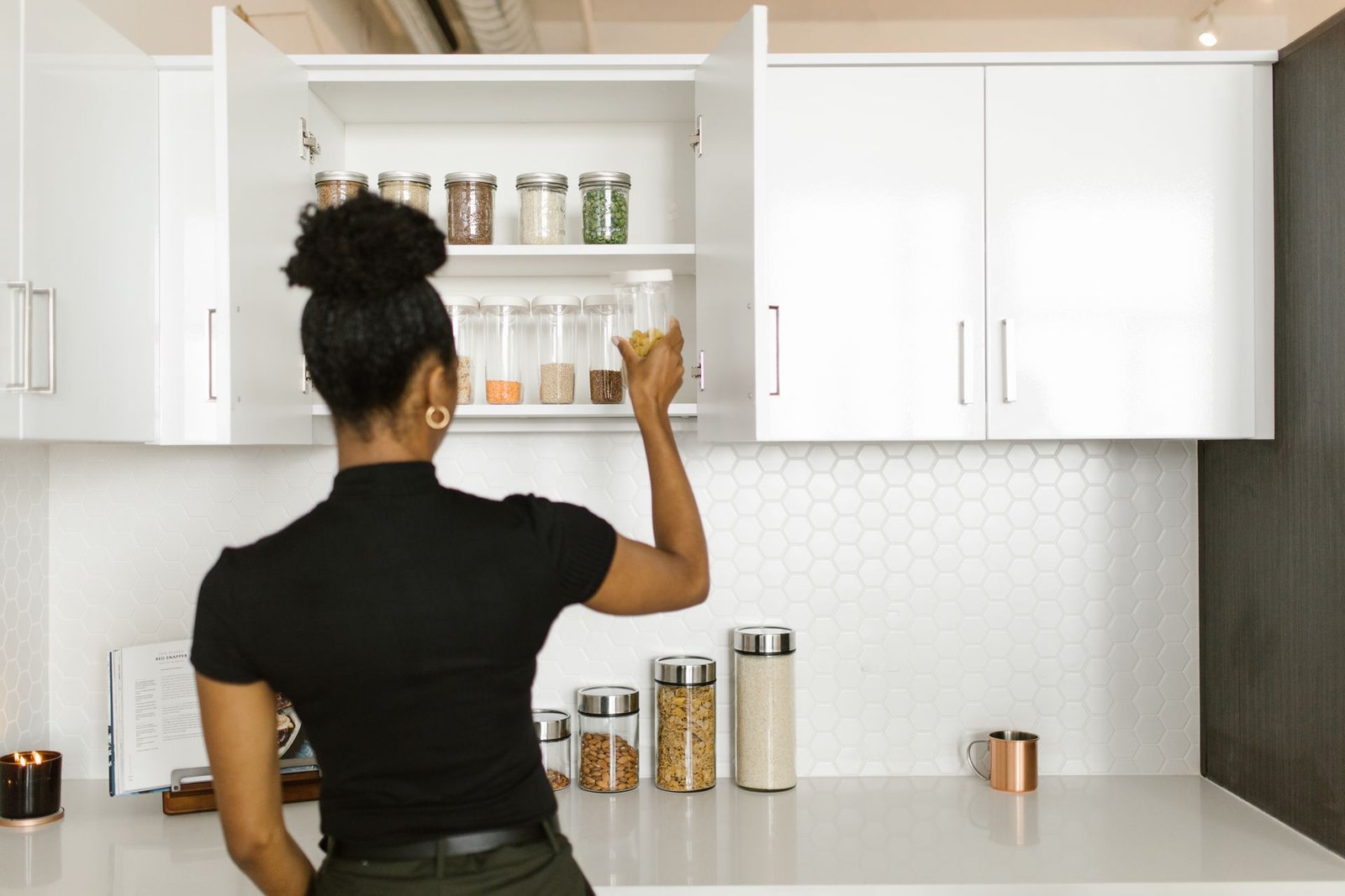 A woman organizing a pantry shelf with various food jars in a mod