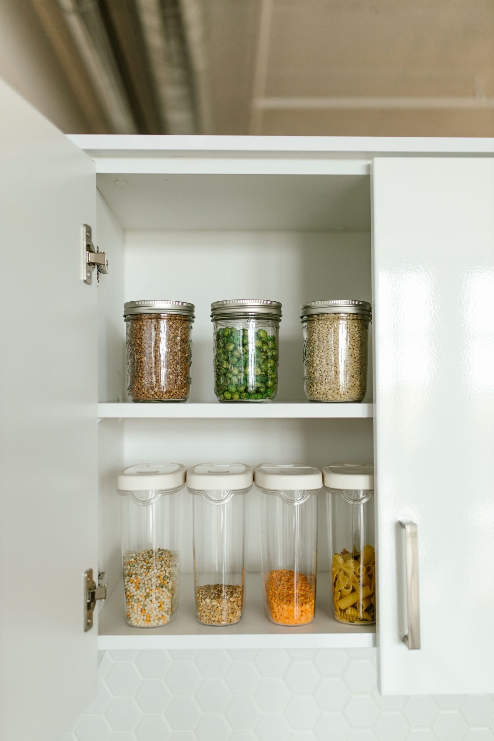 Neatly organized kitchen cabinet with various food items in jars