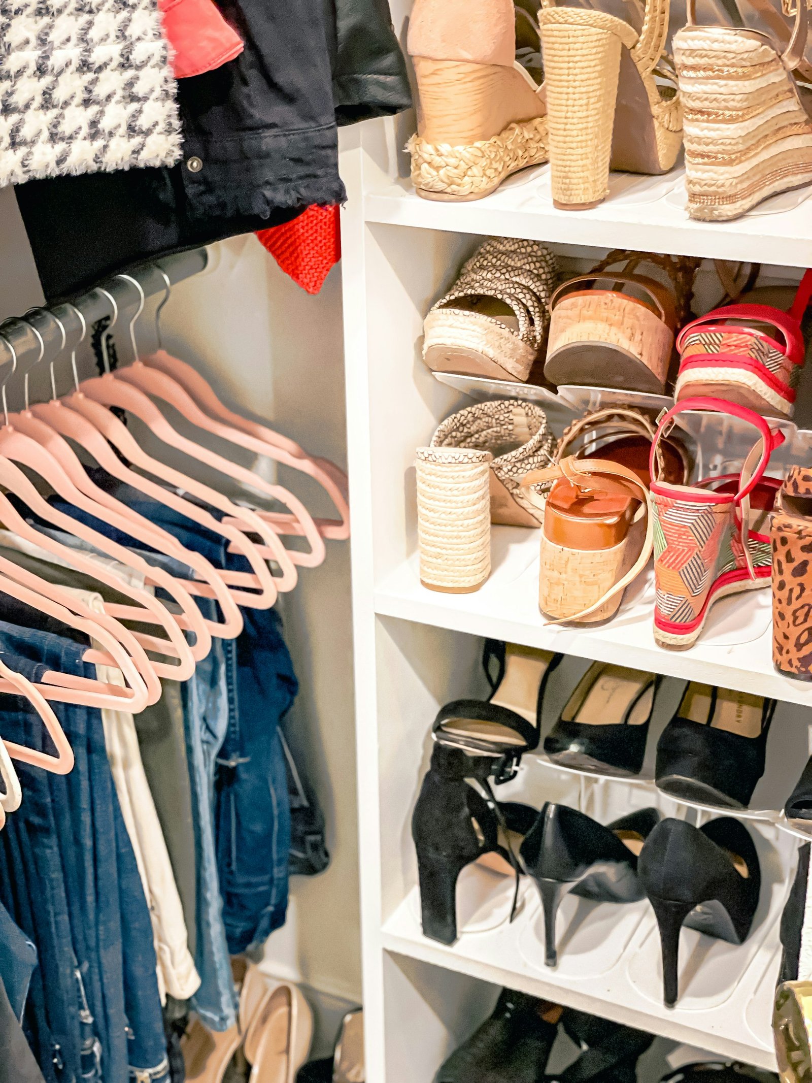 Pink hangers with hanging clothes beside a white shelving unit filled