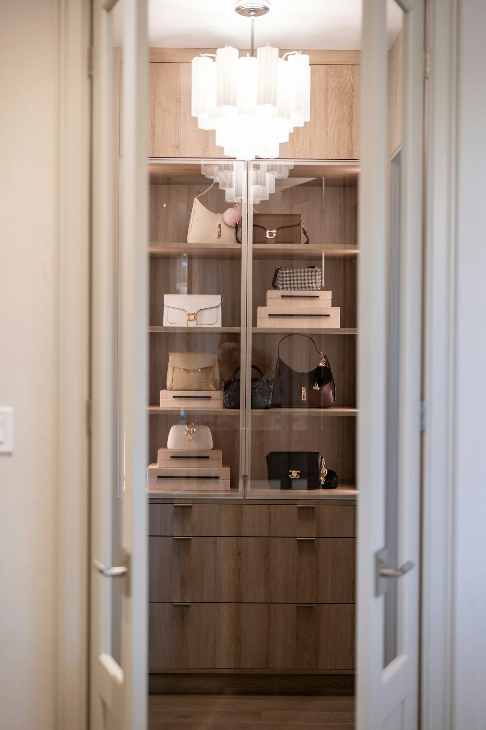 Luxurious closet with handbags and chandelier viewed through open door