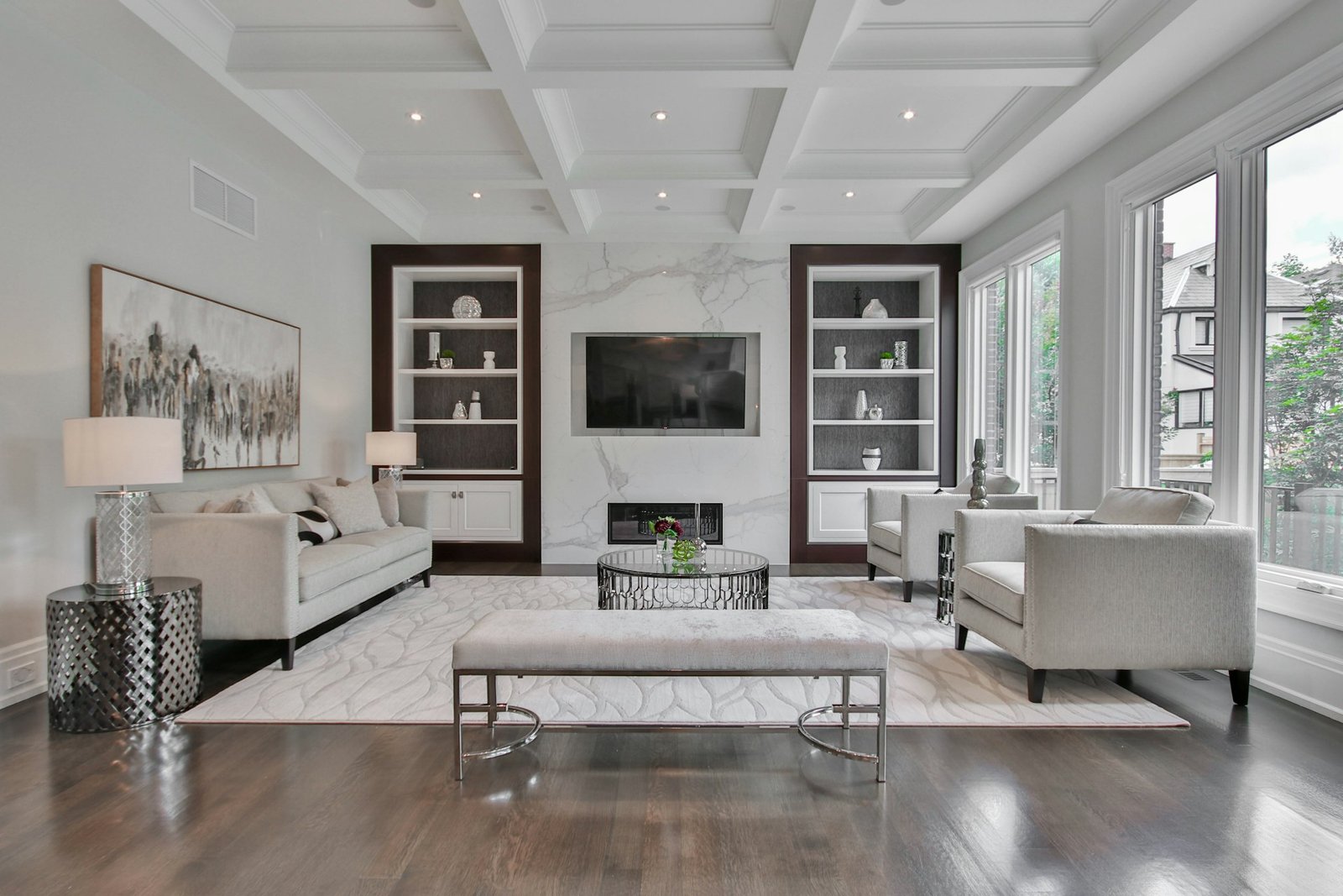 A living room with a marble fireplace, white sofas, and dark wood shel