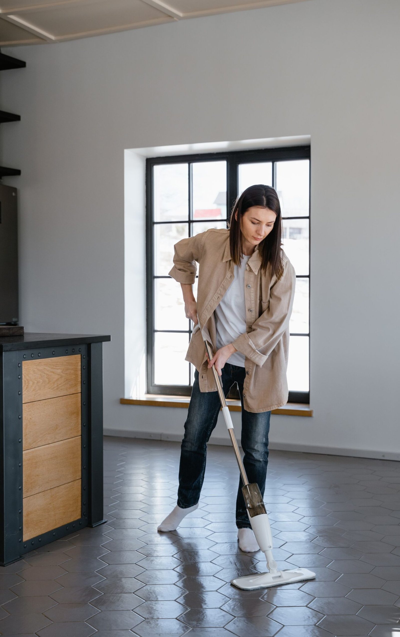Woman cleaning the floor with a mop inside a well-lit modern home