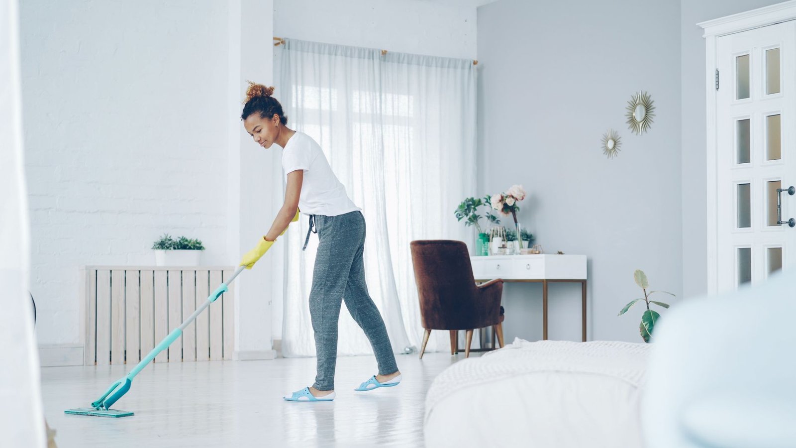 A woman cleaning a bright, modern living room with a mop, creatin