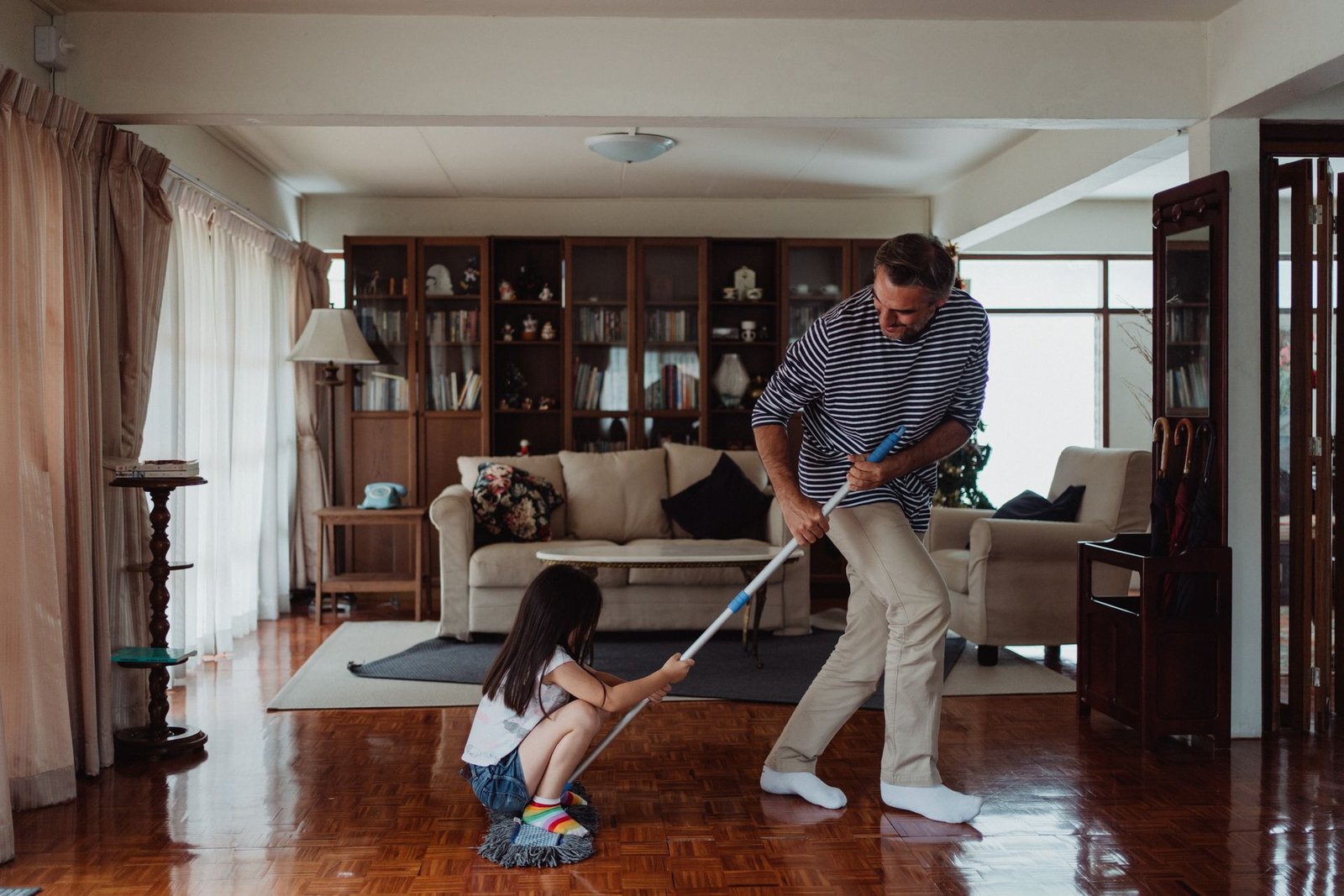 A playful moment as a father and daughter clean their living room