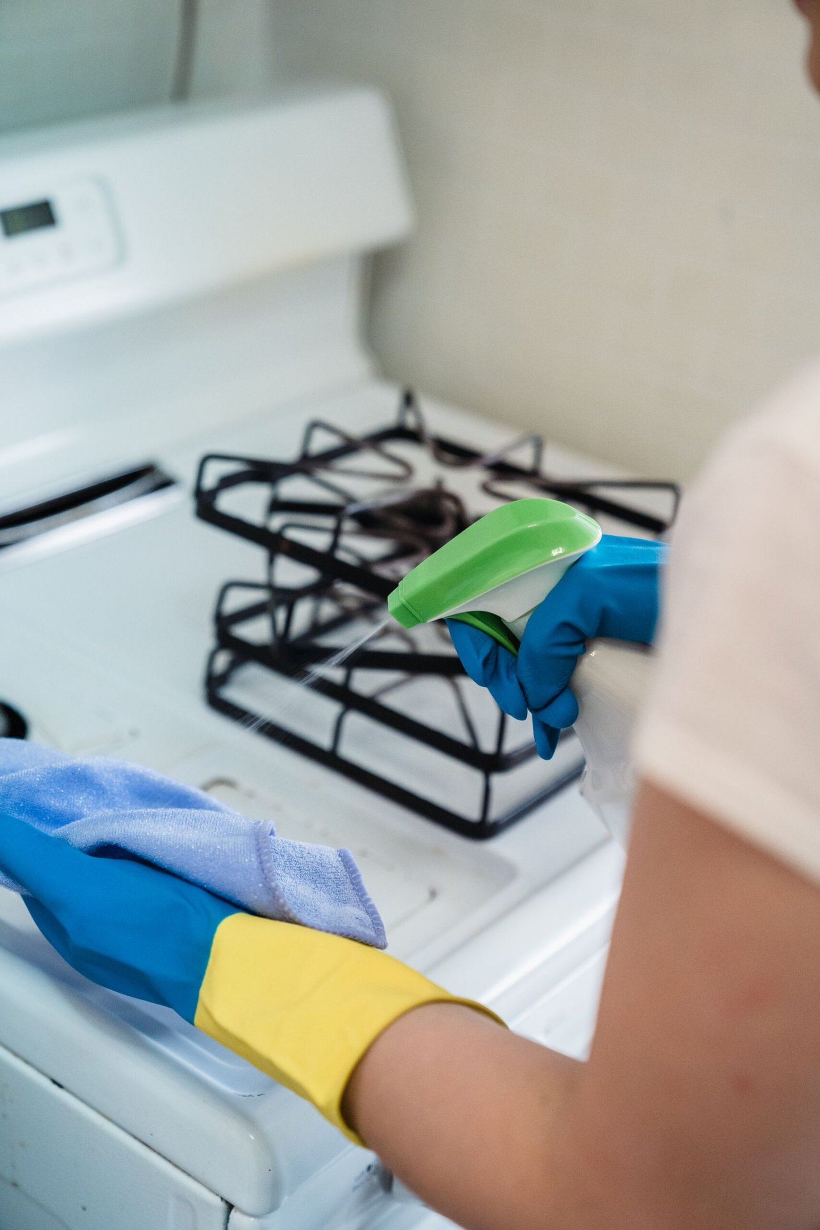 A person wearing gloves uses a spray bottle and cloth to clean a