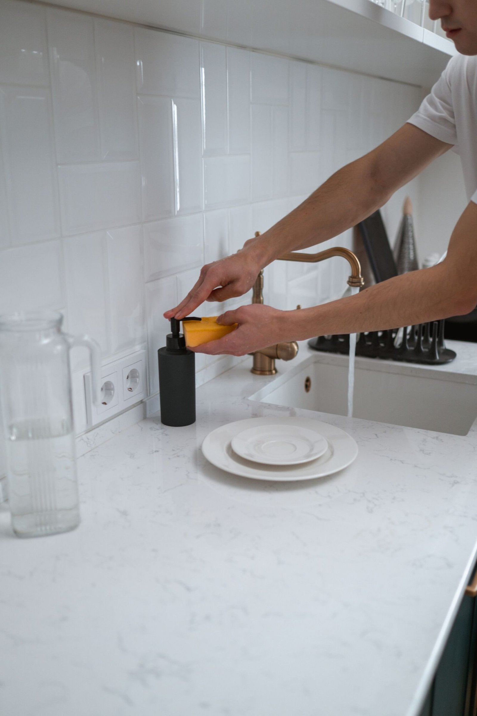 Close-up of hands washing dishes at a modern kitchen sink with wh
