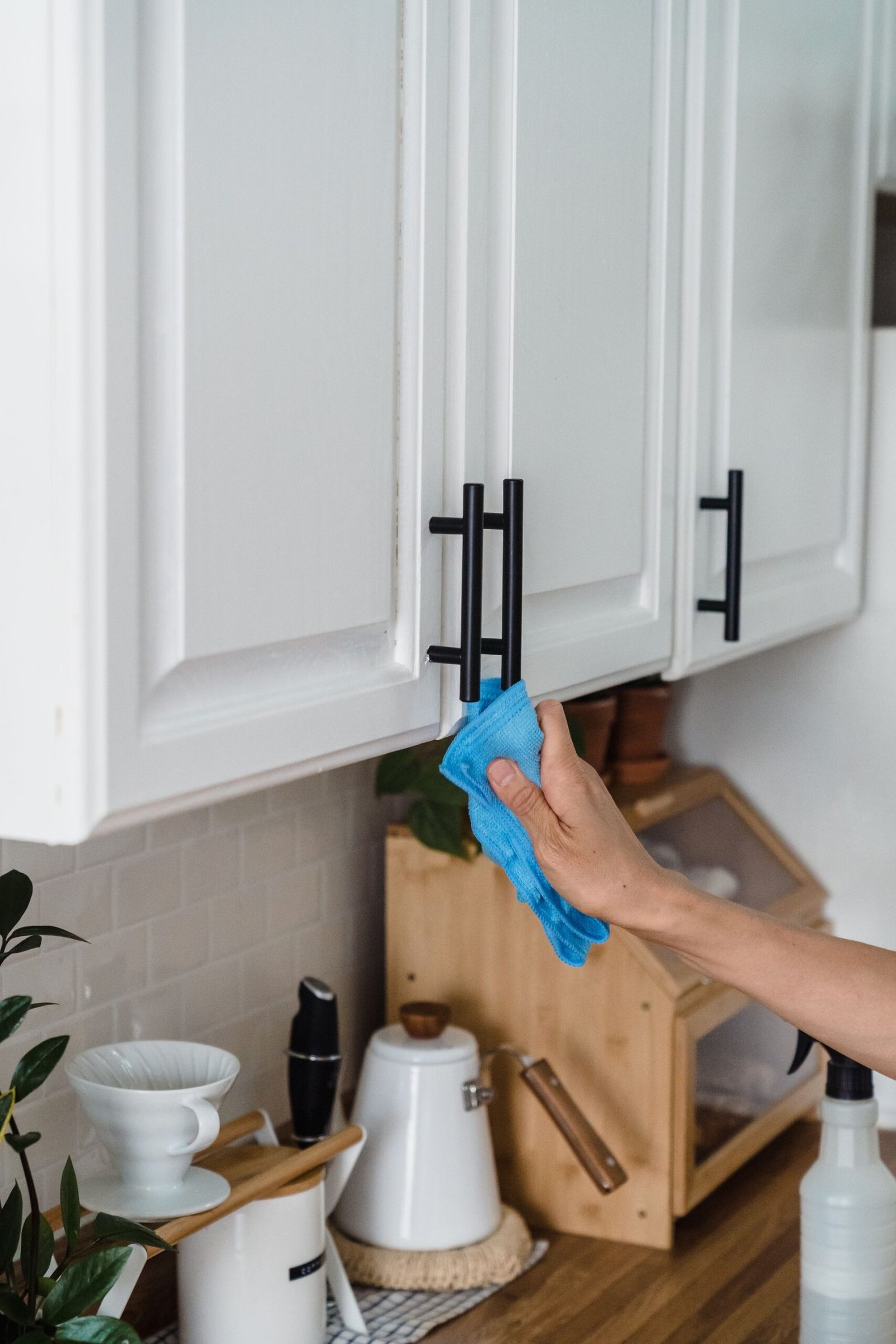 A person using a blue cloth to clean white kitchen cabinets with