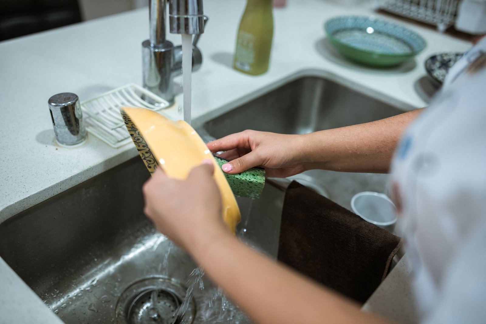 Close-up of hands washing dishes in a kitchen sink with running w