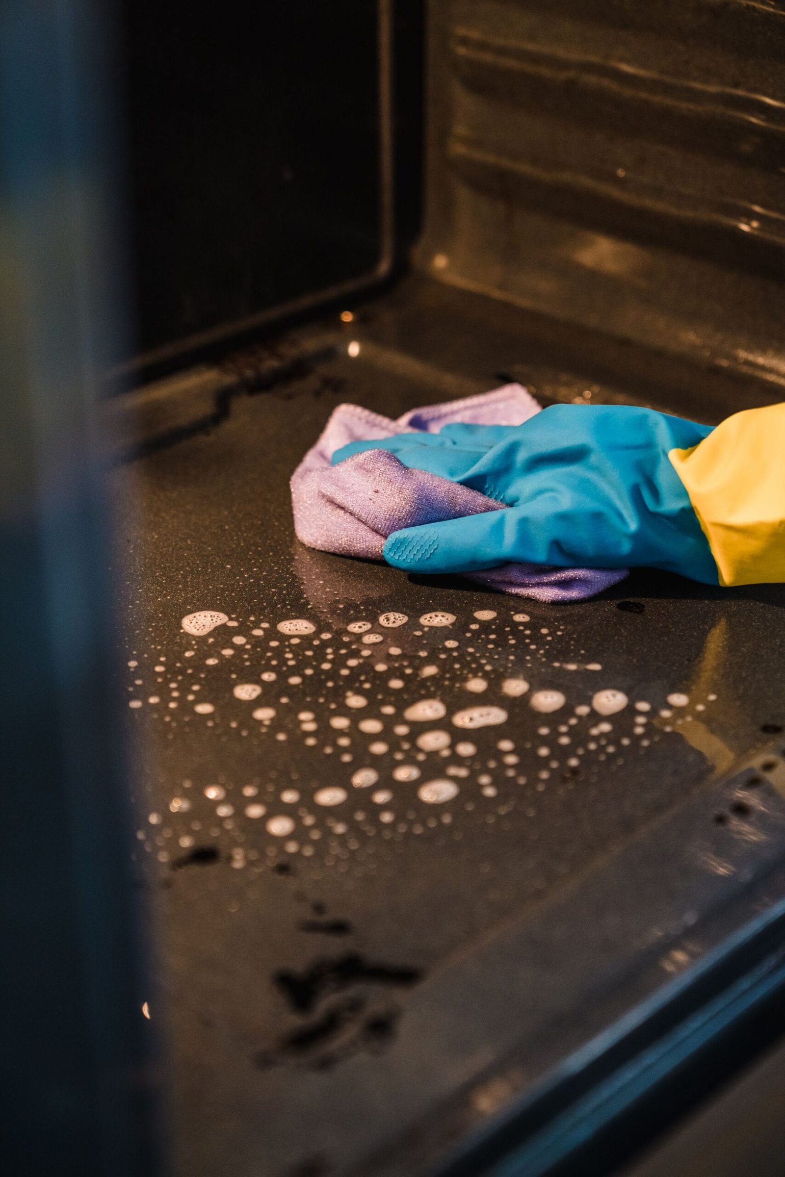 A gloved hand cleans an oven interior using a soapy cloth for a s