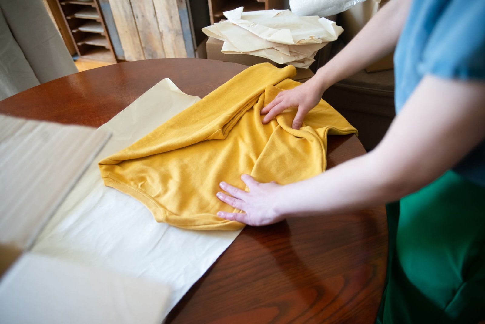 Hands folding a yellow shirt on a wooden table, showcasing a clot