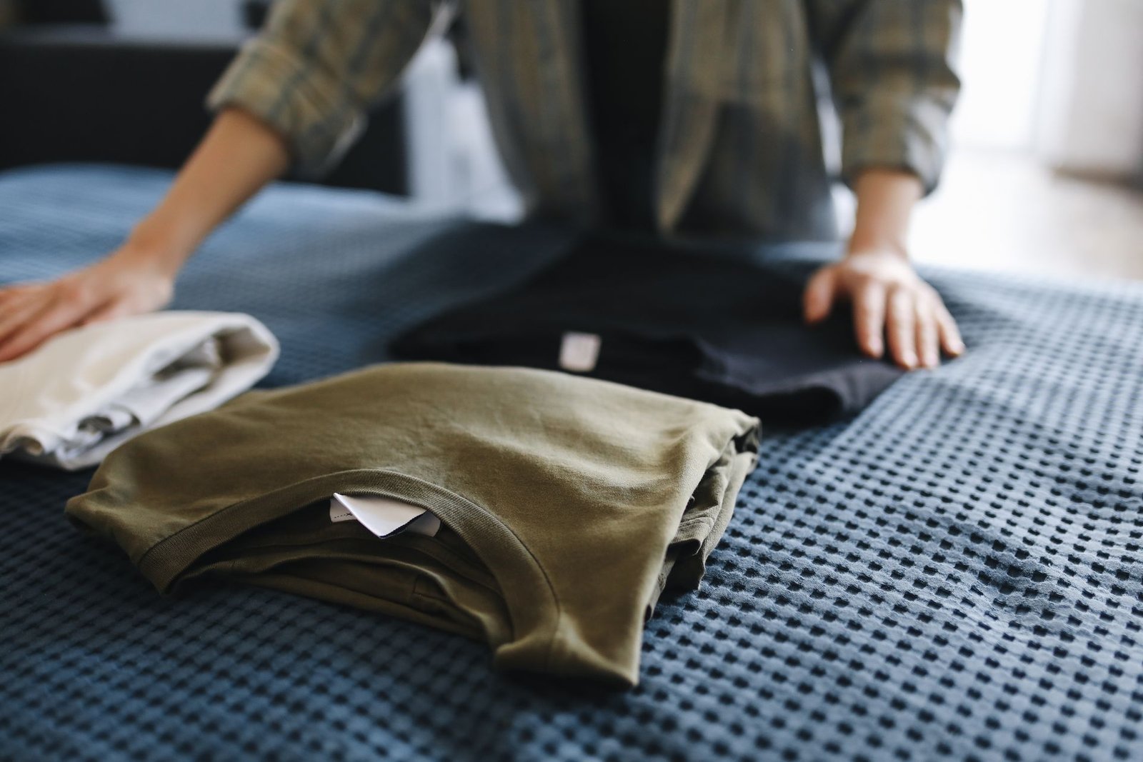 Hands folding T-shirts on a bed, showcasing household chores and