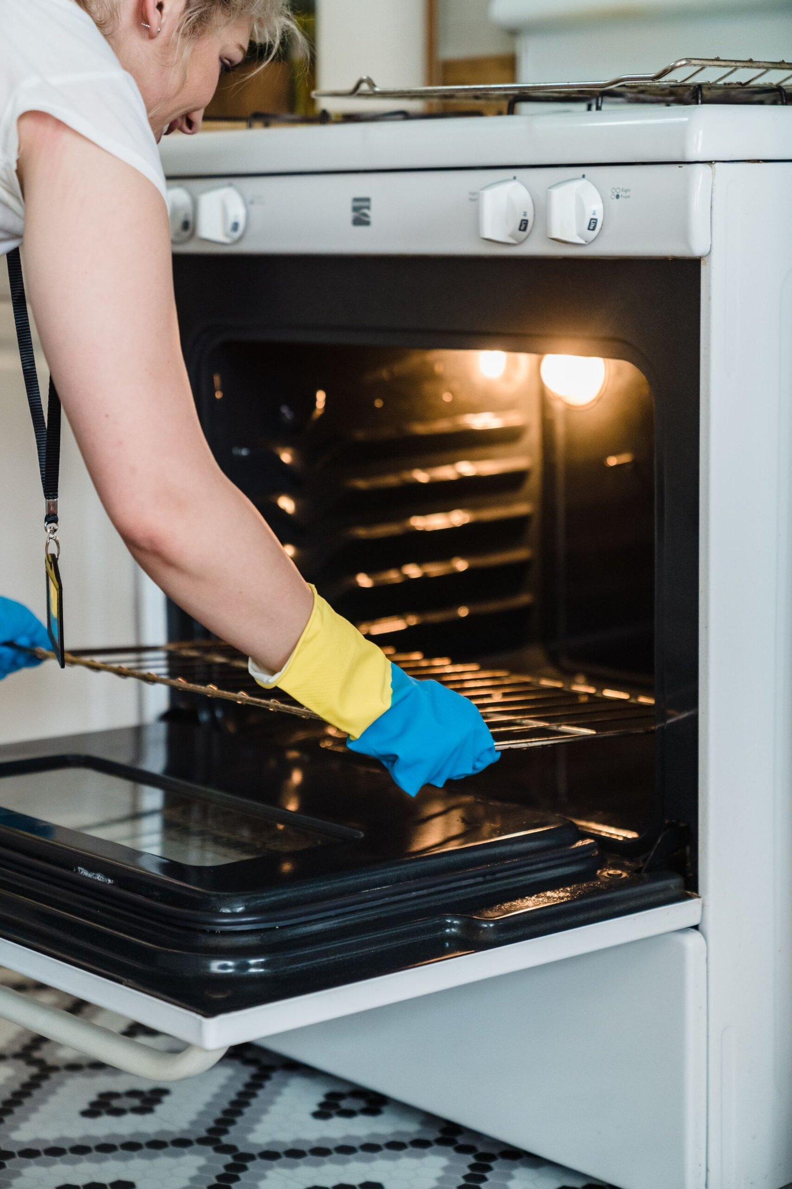 Adult woman cleaning an oven using protective rubber gloves indoo