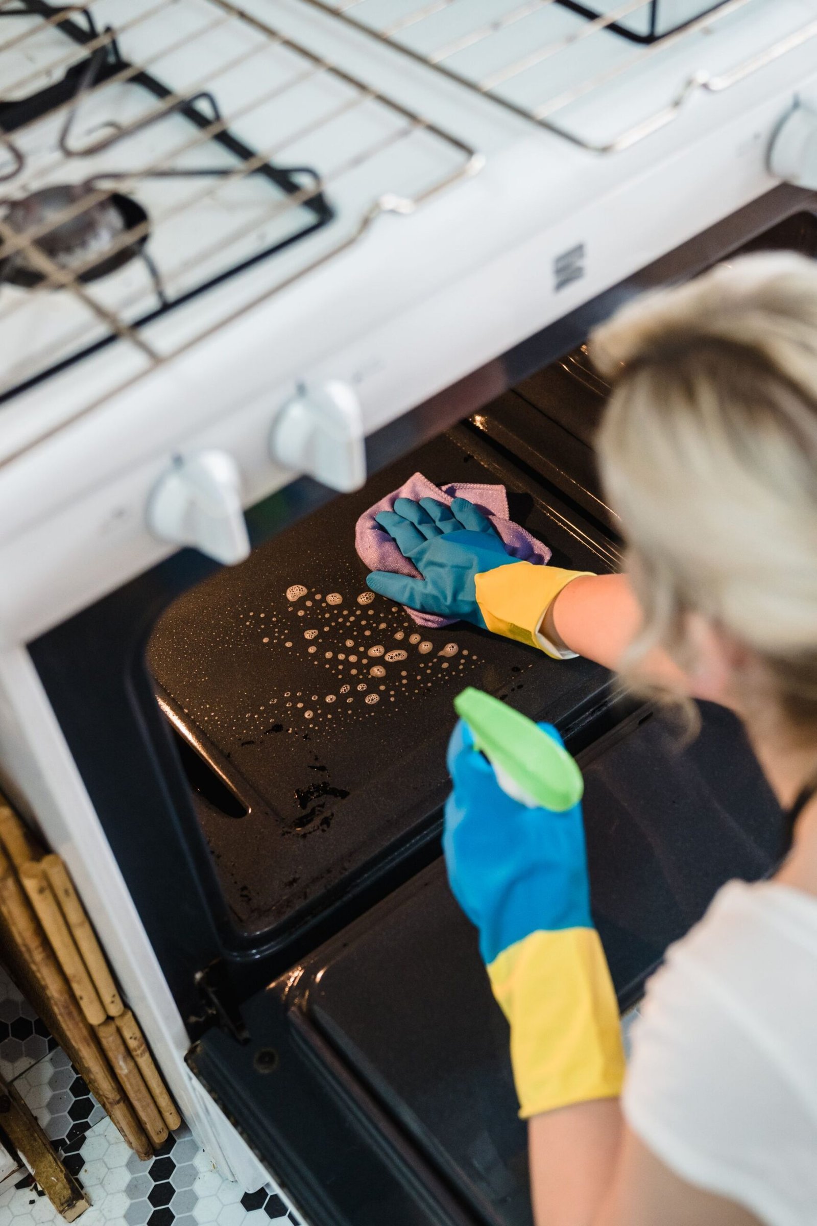 A woman wearing gloves cleans an oven in a domestic kitchen setti