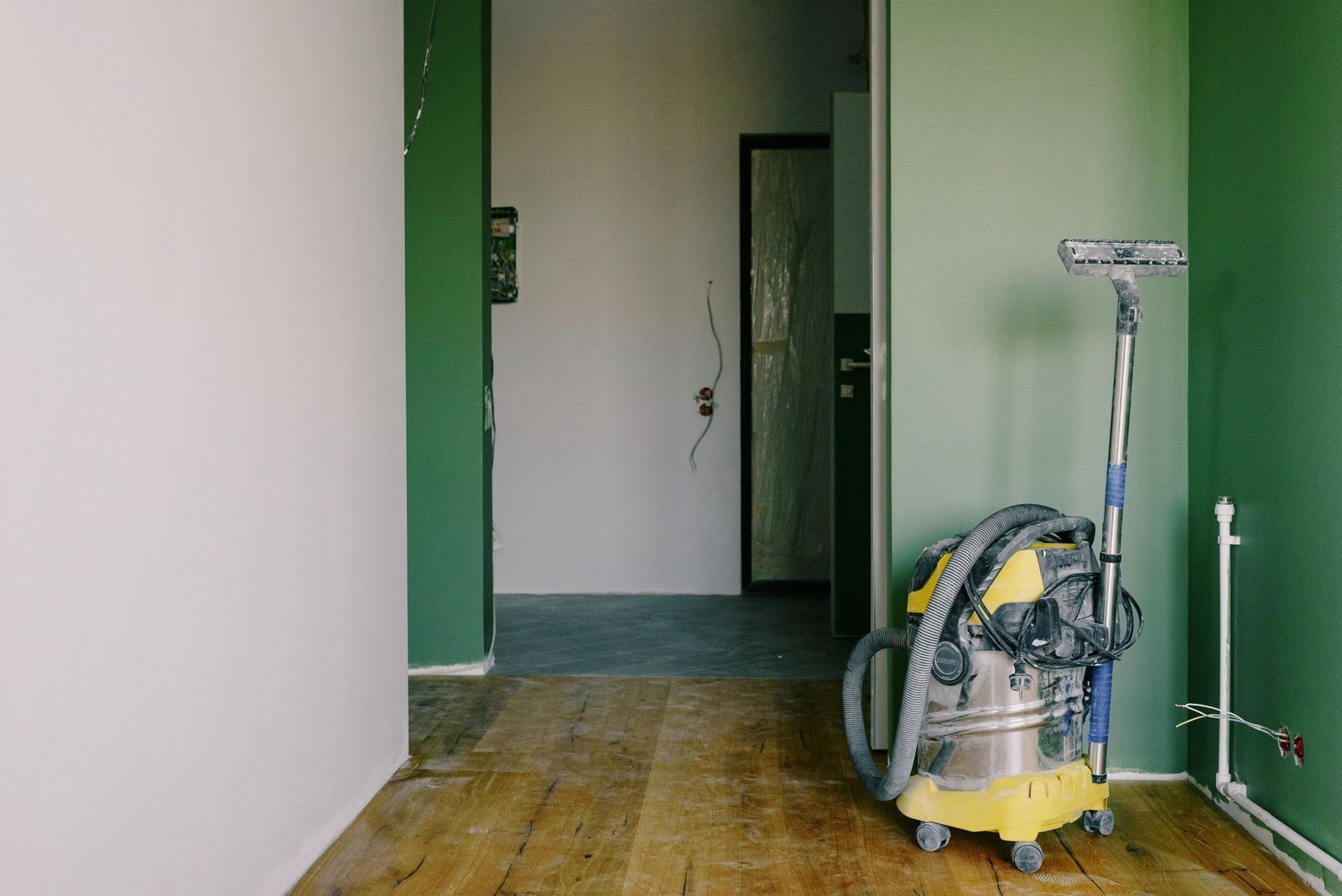Industrial vacuum cleaner placed on dirty parquet in room with gr