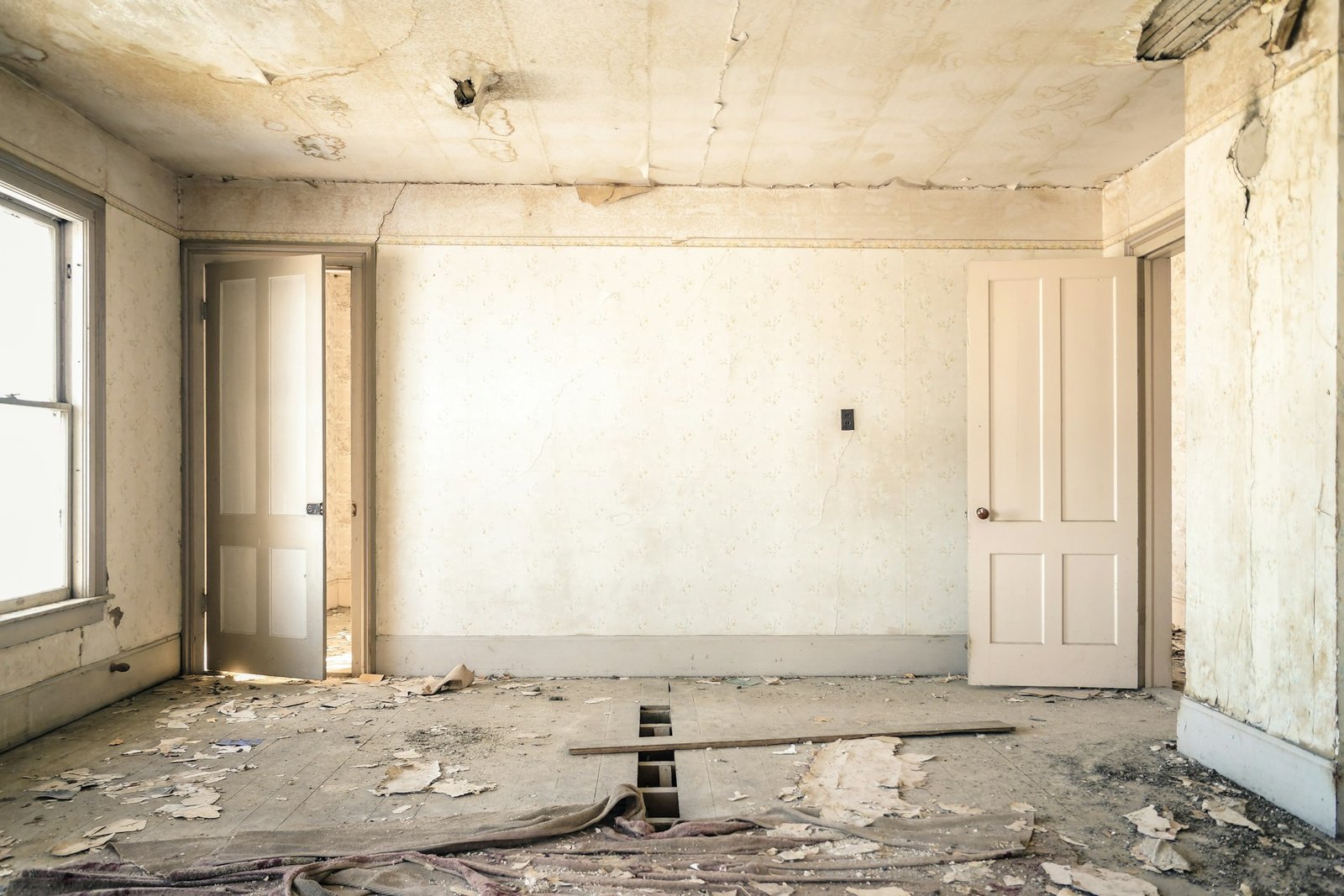 An abandoned room with peeling wallpaper, two open doors, and a damage