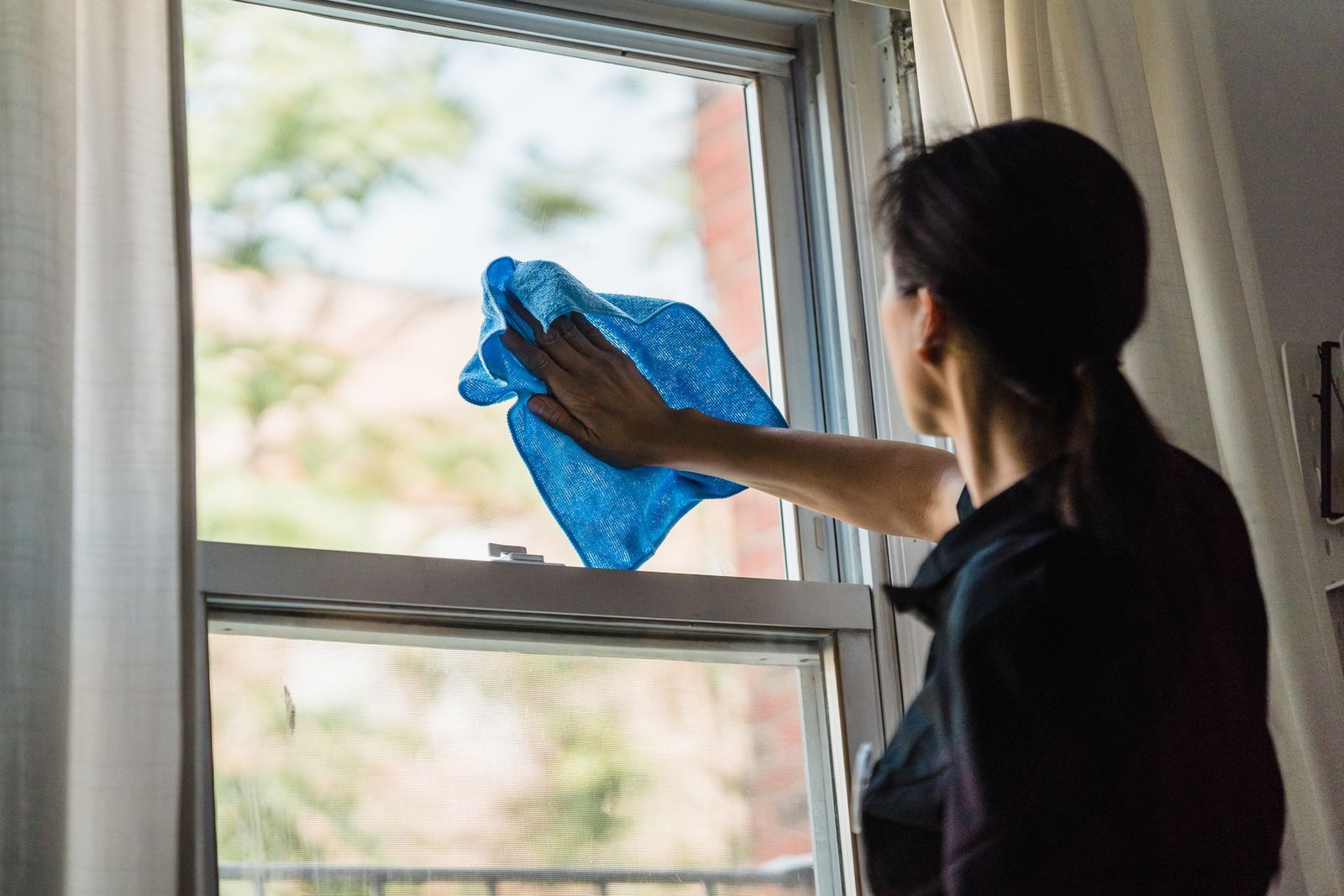 A woman cleans a window using a blue microfiber cloth providing a