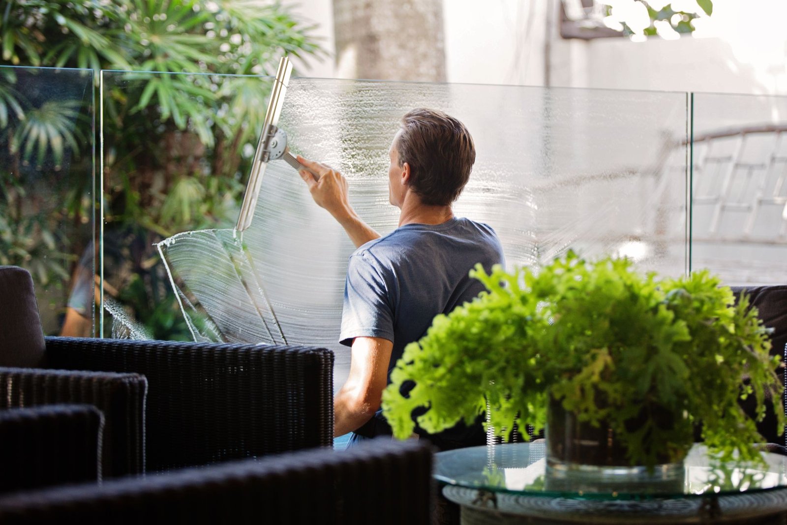 A man cleaning a glass barrier outdoors with a squeegee, surround