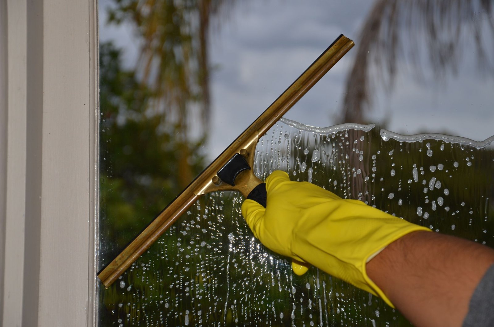 Close-up of hand cleaning window with squeegee outdoors using yel